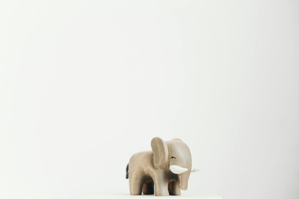 A minimalist wooden elephant toy set against a bright white background, offering ample copyspace.