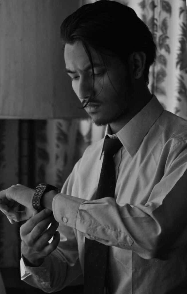 Stylish man in black and white adjusting his watch indoors, portraying elegance.