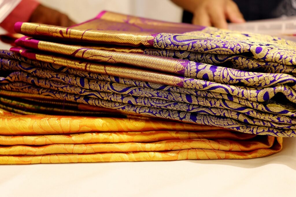 A stack of luxurious Kanchipuram silk sarees showcasing intricate patterns and vibrant colors.