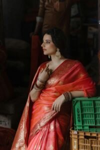 A thoughtful woman in a vibrant saree exudes elegance and grace indoors.