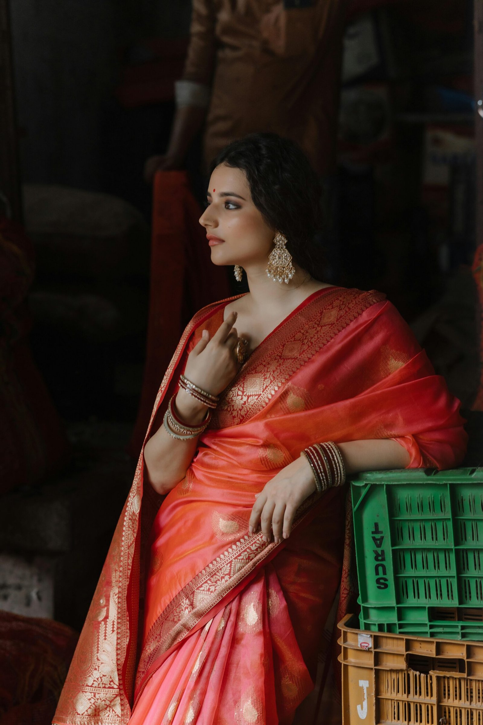 A thoughtful woman in a vibrant saree exudes elegance and grace indoors.