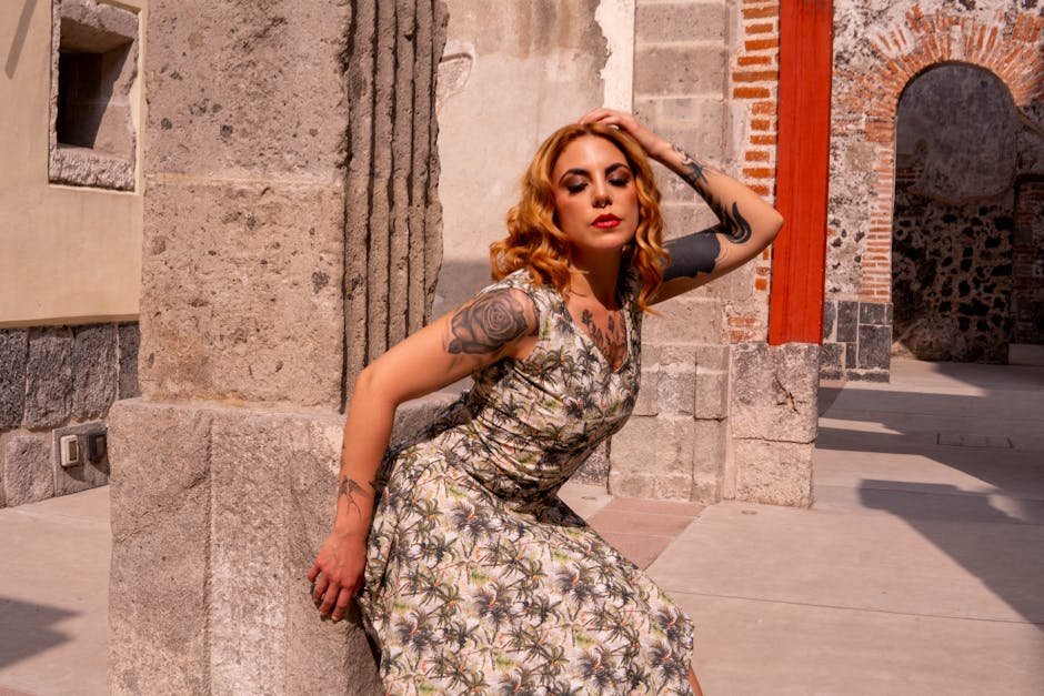Stylish woman with tattoos poses against ancient architecture, embracing modern fashion.