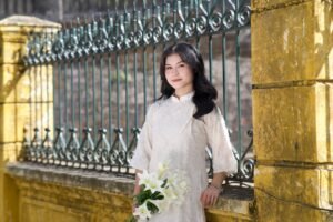 Woman standing by a historic fence in traditional dress holding flowers.