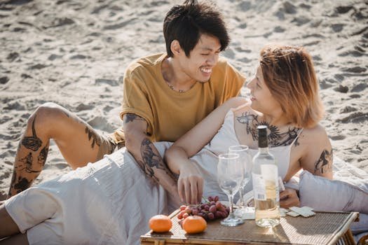 A couple enjoying a romantic picnic on a sunny beach, relaxing and sharing a joyful moment together.